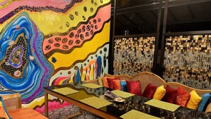 A vibrant room with a colorful abstract mural, a woven wall hanging, and a sofa with colorful cushions.