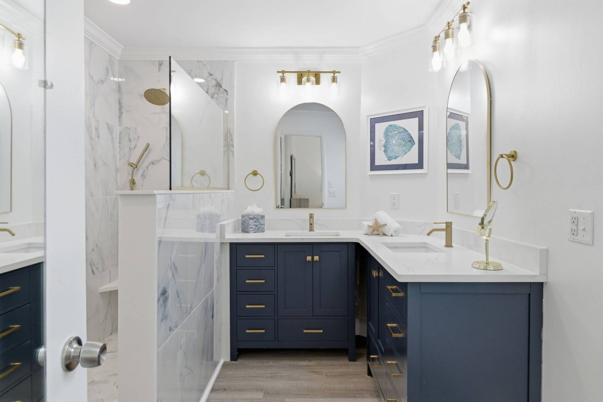 A modern bathroom with marble walls, a shower, two sinks, and dark blue cabinets.
