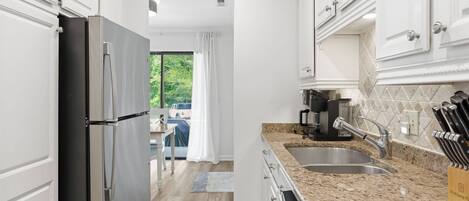 A modern kitchen with white cabinetry, a granite countertop, a stainless steel sink, and a coffee maker.