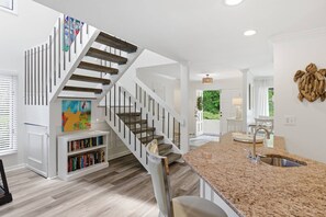 Une cuisine moderne dotée d’un plan de travail en granit et d’un évier en acier inoxydable, d’un escalier avec des marches en bois et des rampes en métal, et d’une bibliothèque remplie de livres.