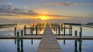 Eine Holzstege, der sich in ruhiges Wasser erstreckt, mit einem Sonnenuntergang im Hintergrund.