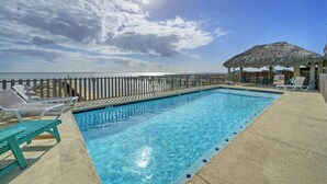 Une piscine avec des chaises longues et une structure dotée d’un toit de chaume.