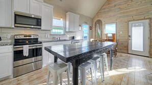 Une cuisine moderne dotée d’appareils électroménagers en acier inoxydable, d’un grand îlot central avec des tabourets et d’un revêtement de sol en bois.