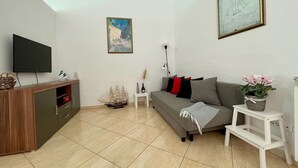 A modern living room with a flat-screen TV, a wooden cabinet, a grey sofa, a small table with a vase, and a painting on the wall. - Spacious Apartment in Istrian Stone House with terrace and private parking space (Vabriga)