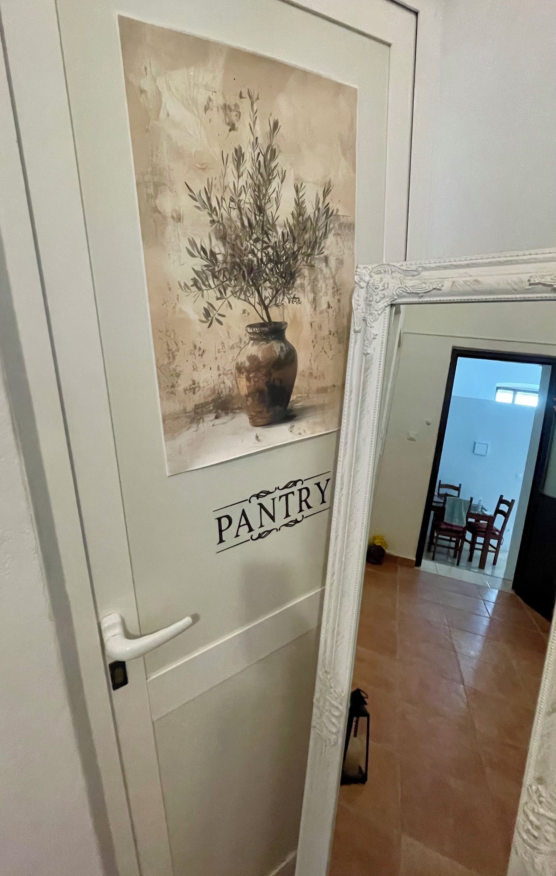 A door with a 'PANTRY' sign and a vintage-style painting of a plant in a vase.