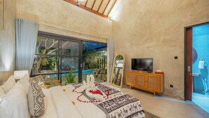 A bedroom with a large bed, a TV, a wooden cabinet, and a view of an outdoor pool. - Villa Jonsu Uluwatu by Nagisa Bali (Ungasan)