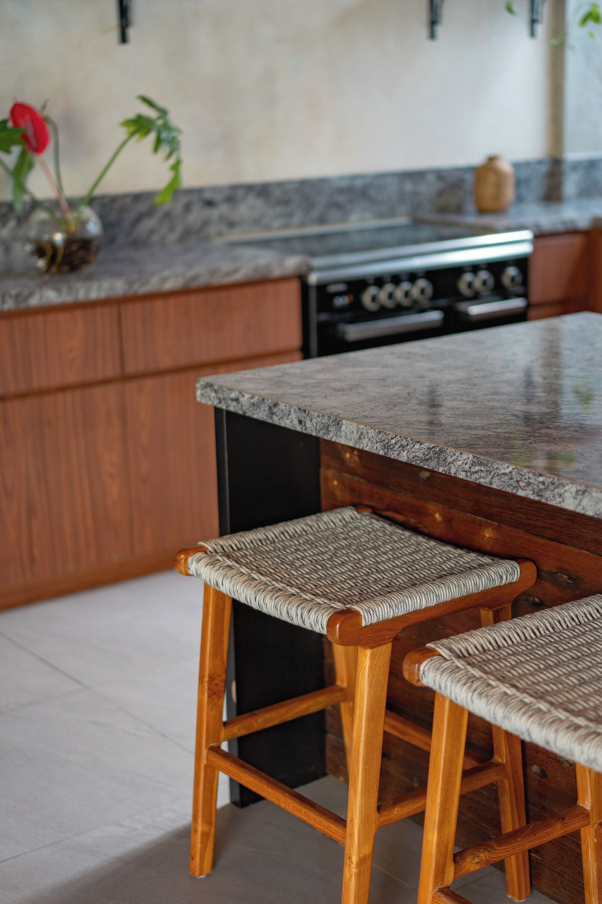 A kitchen with wooden cabinets, a granite countertop, and two wicker stools.