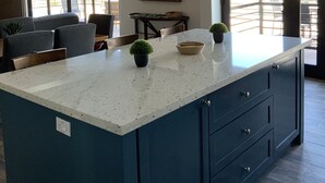 Een moderne keuken met een groot eiland, donkere kastjes en een eethoek met uitzicht.