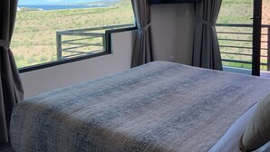 Een slaapkamer met een groot bed, een aan de muur bevestigde televisie en een balkon met uitzicht op het landschap.