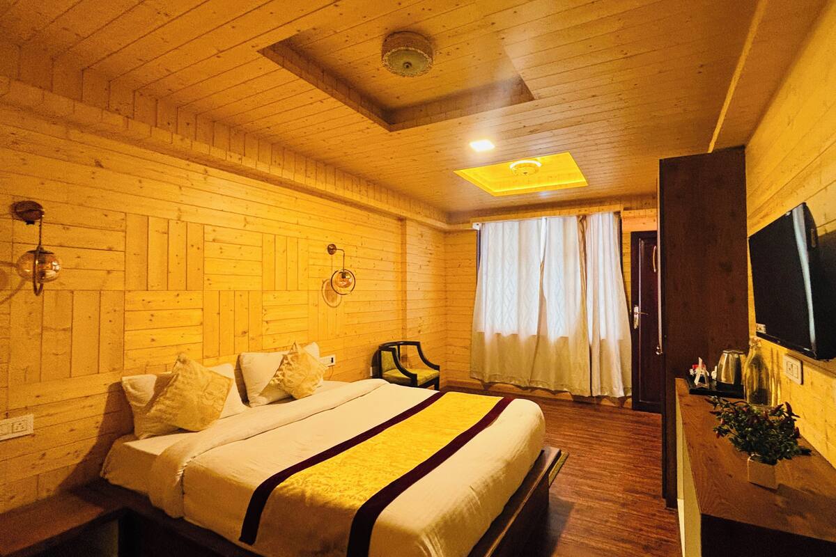 Een kamer met houten lambrisering, een bed, een stoel, een televisie en een raam met gordijnen.