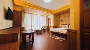A wooden-floored room with a bed, a table, and a chair.