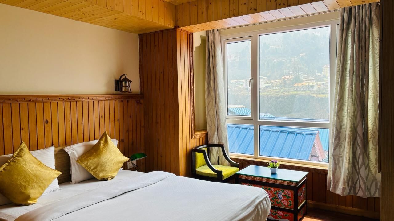 A room with a bed, a chair, a small table, and a window with a view of buildings.