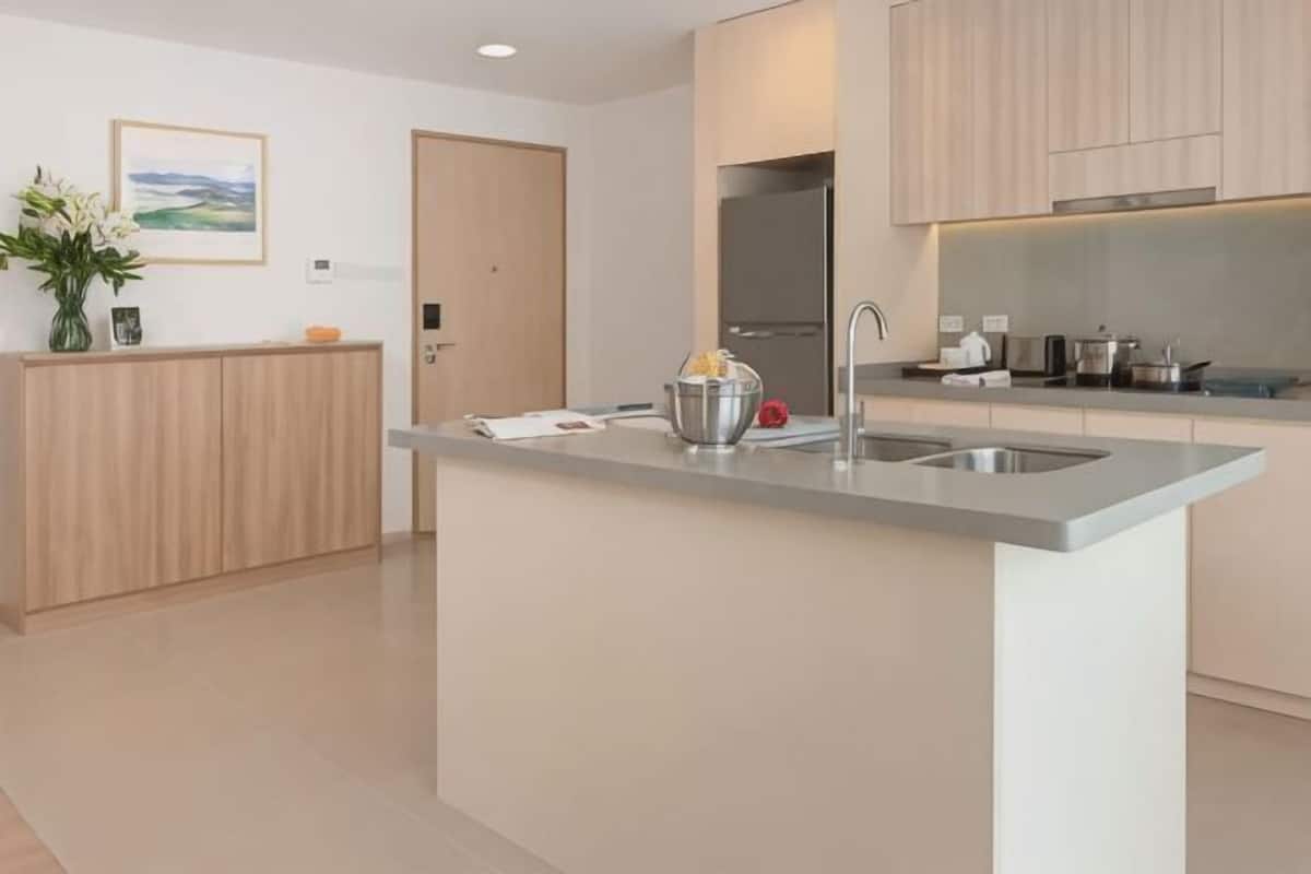 Uma cozinha moderna com ilha central, eletrodomésticos de aço inoxidável e armários em madeira clara.