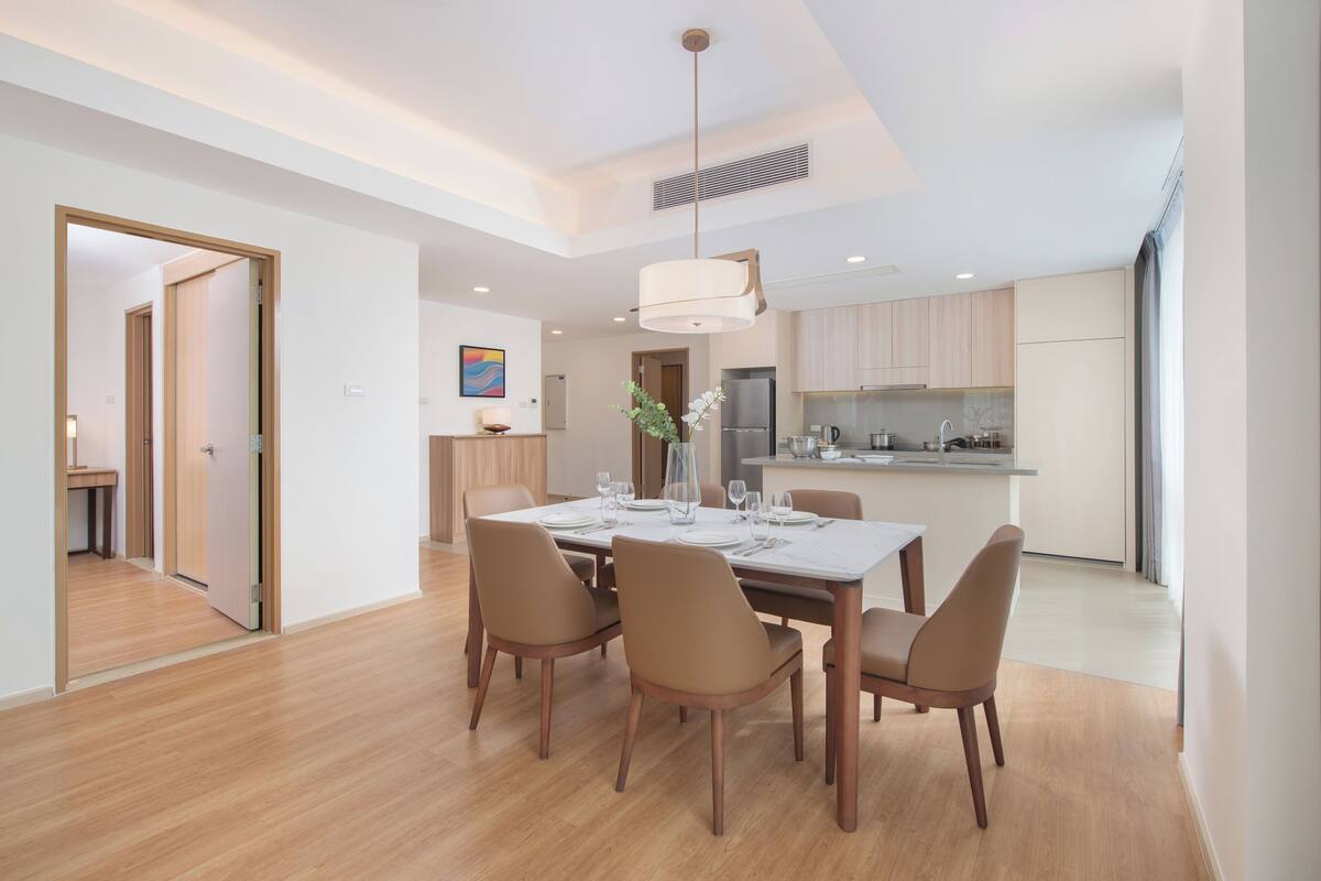 Uma área de refeições moderna com uma mesa e cadeiras de madeira, uma cozinha ao fundo e um corredor que dá para outro quarto.