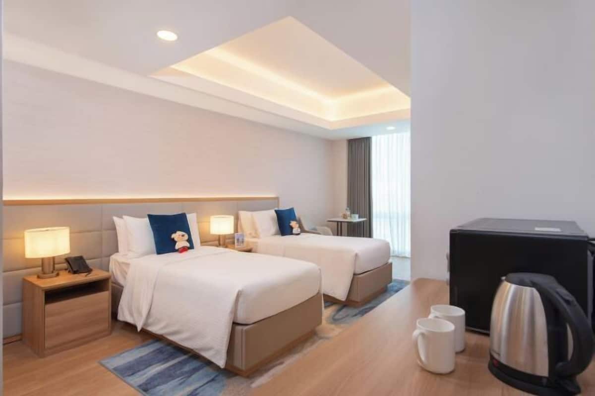 Quarto de hotel com duas camas, uma escrivaninha, uma cafeteira e uma chaleira.
