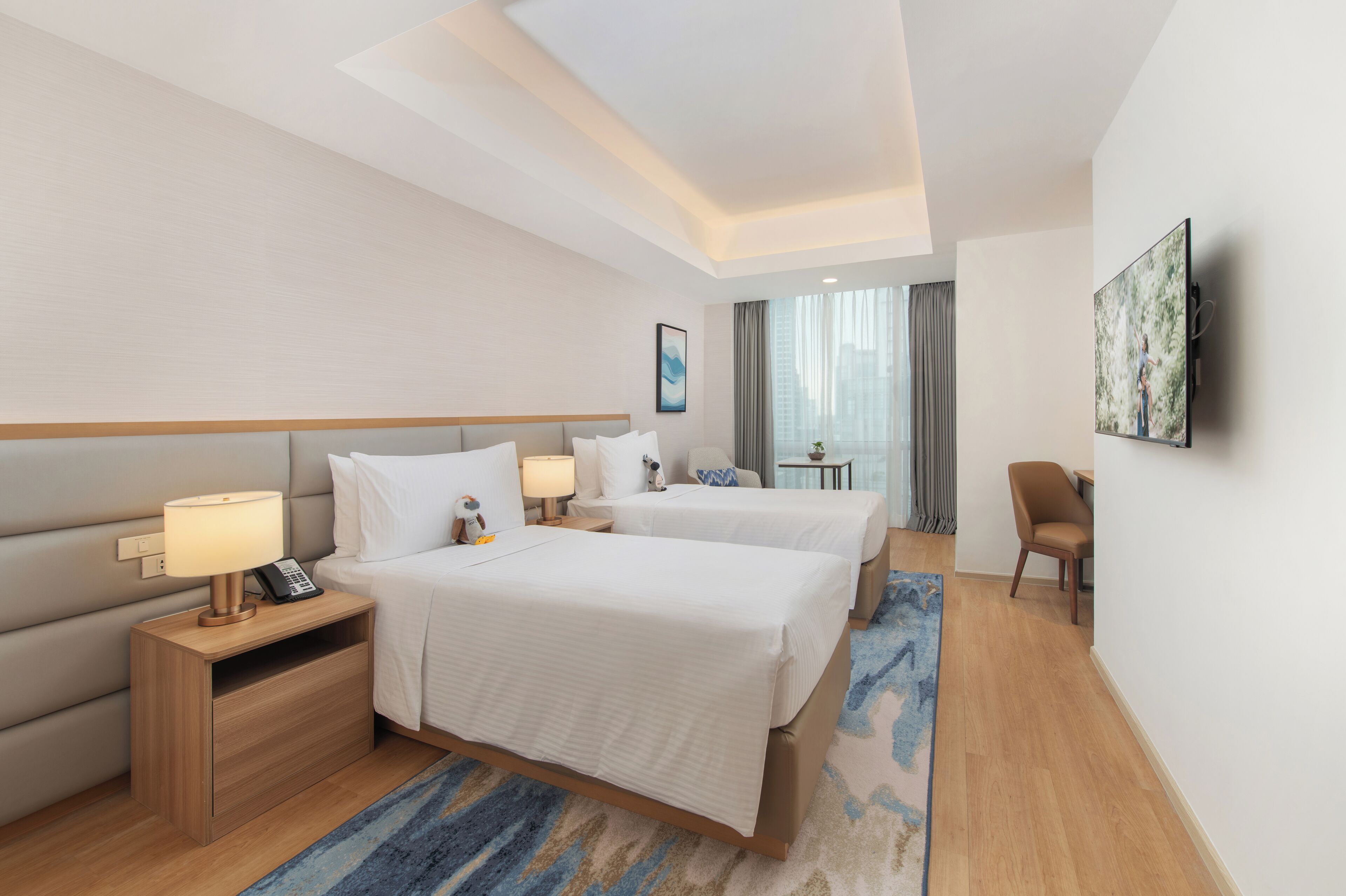 Habitación de hotel con dos camas, un escritorio, una silla, un televisor y una ventana con cortinas.