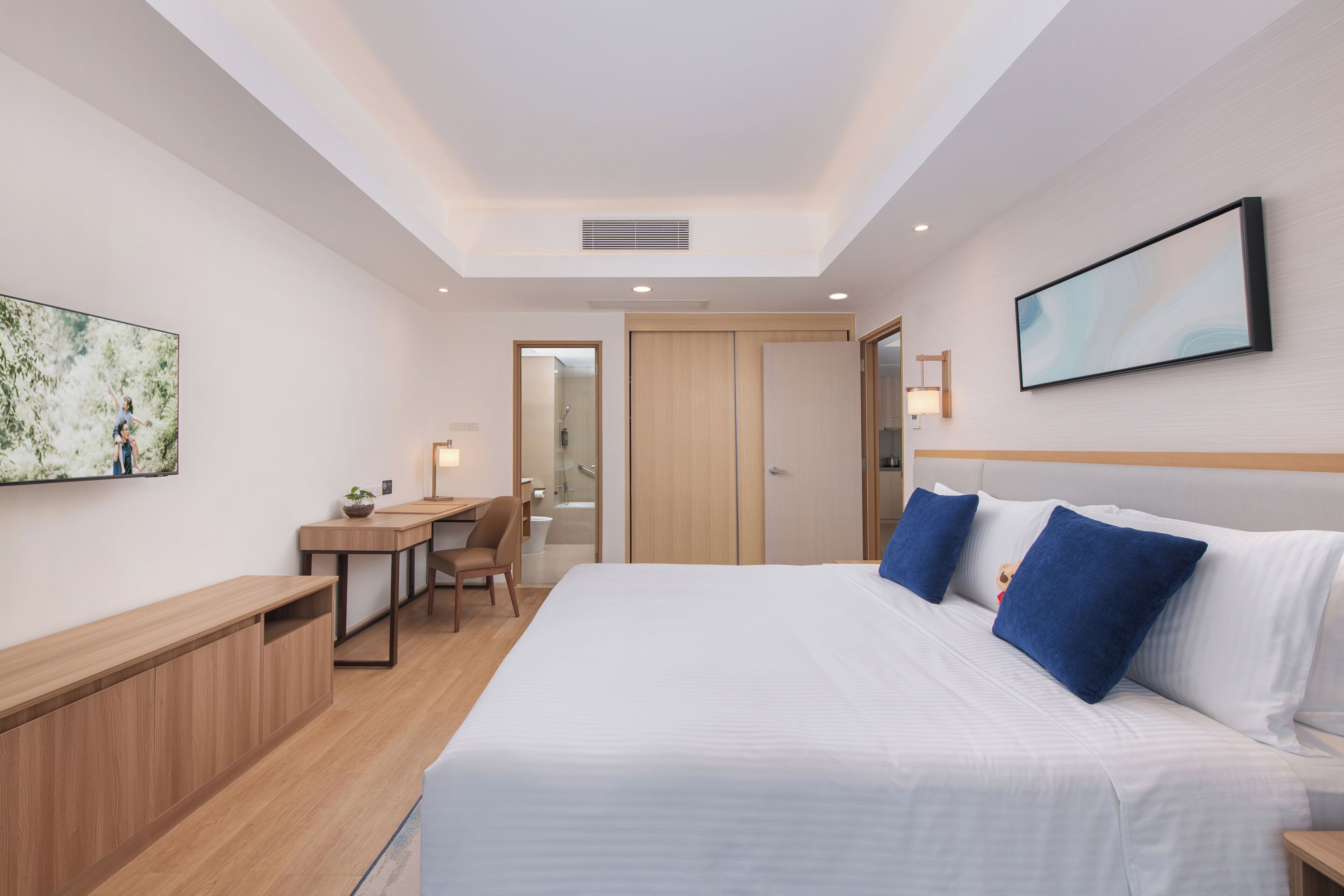 A hotel room with a bed, a desk, a chair, a TV, and a door leading to a bathroom.