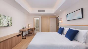 A hotel room with a bed, a desk, a chair, a TV, and a door leading to a bathroom.