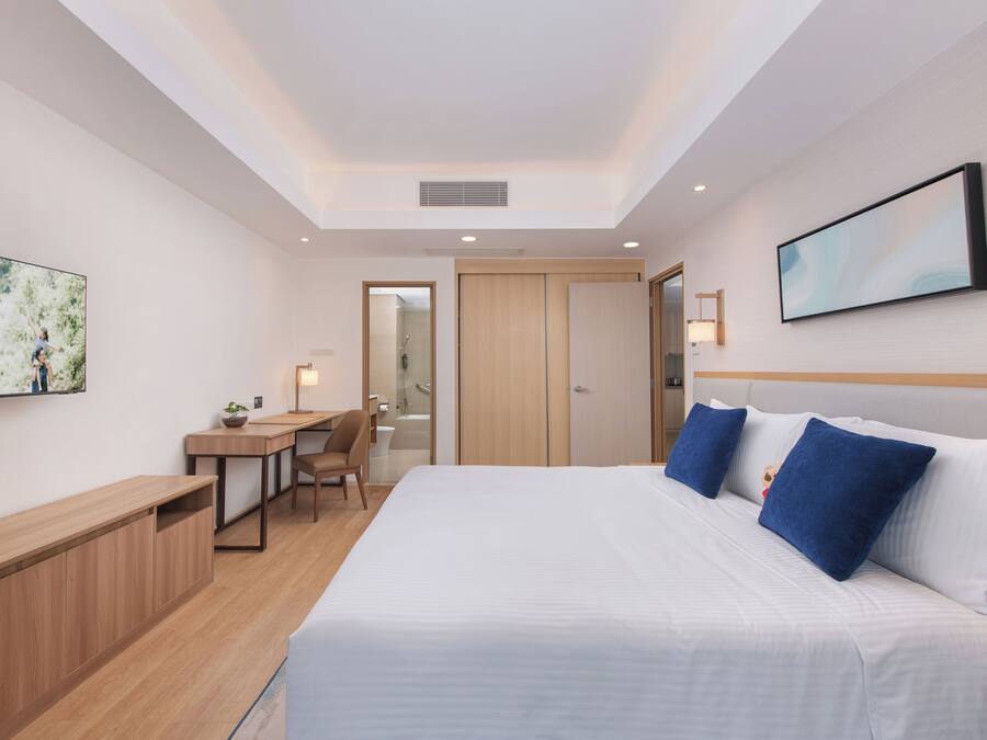 A hotel room with a bed, a desk, a chair, a TV, and a door leading to a bathroom.