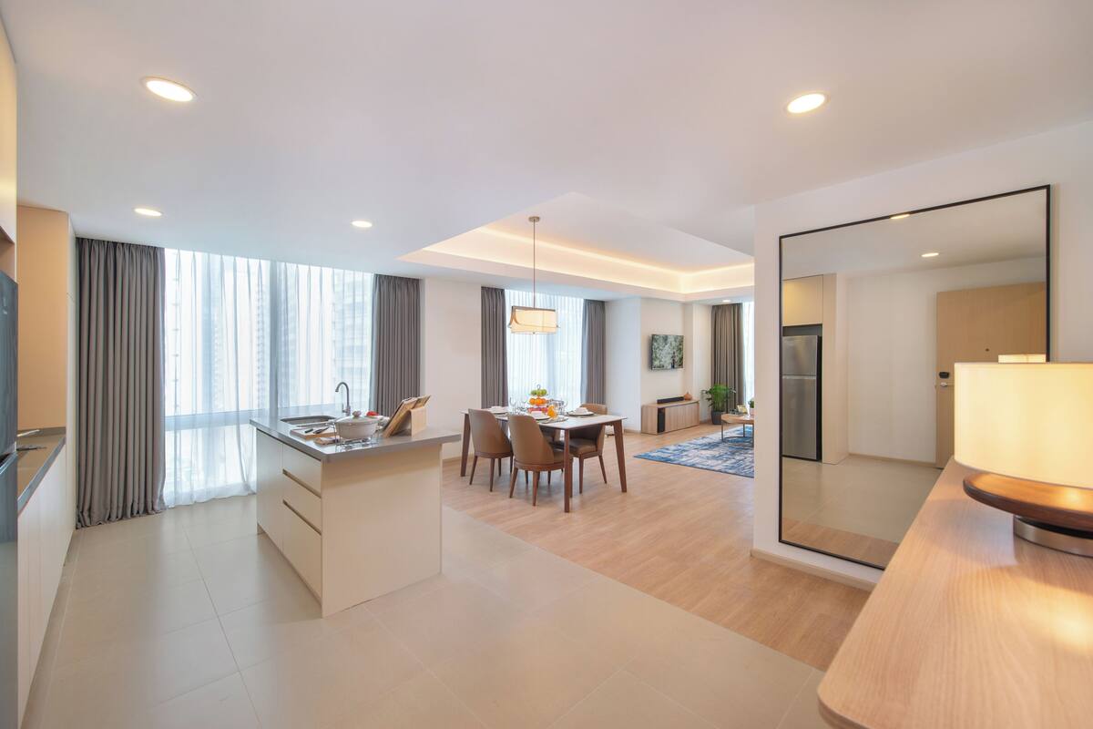 Quarto de hotel moderno com área de refeições, cozinha e um espelho grande.