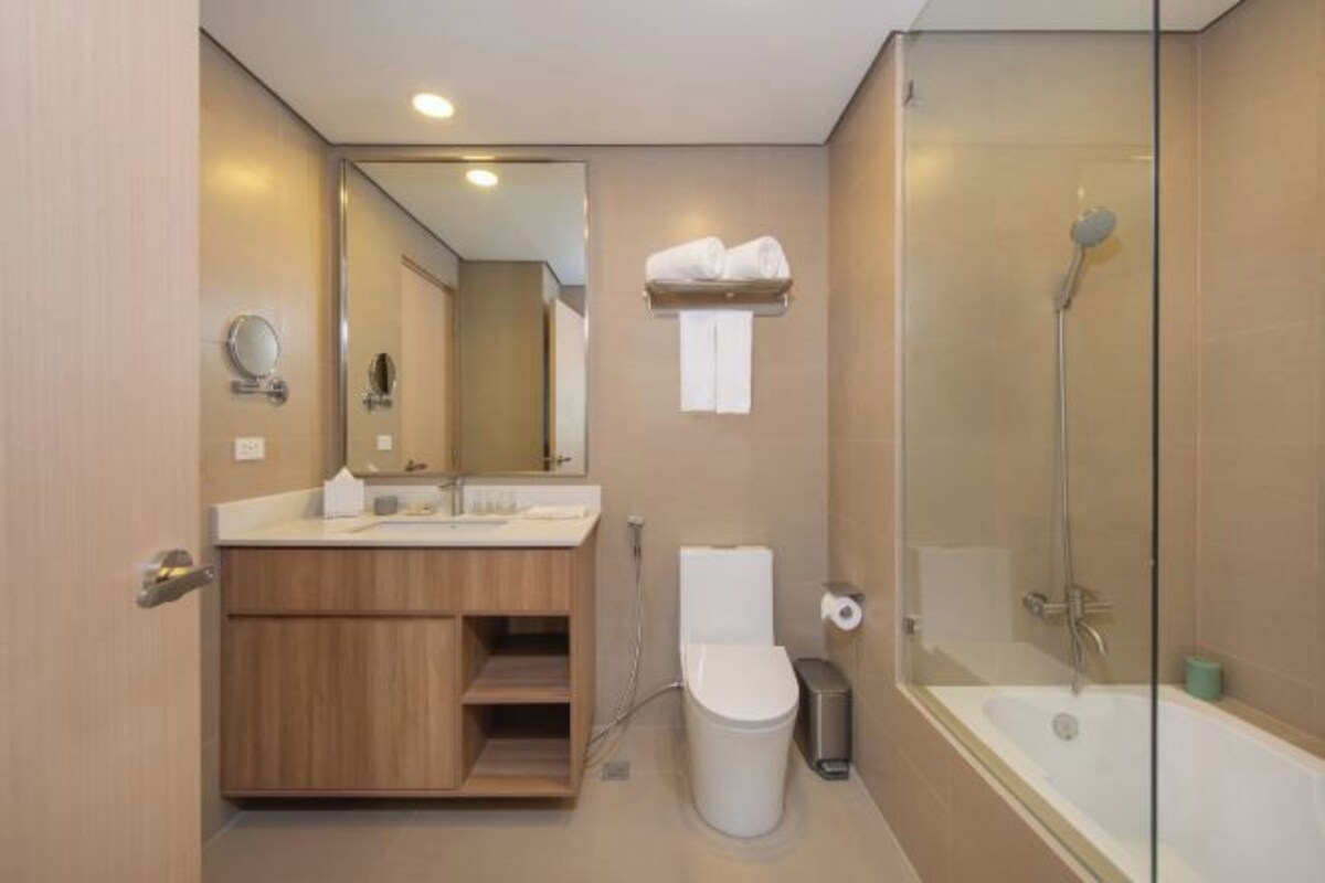 A modern bathroom with a glass shower enclosure, a wooden vanity, a toilet, and a bathtub.
