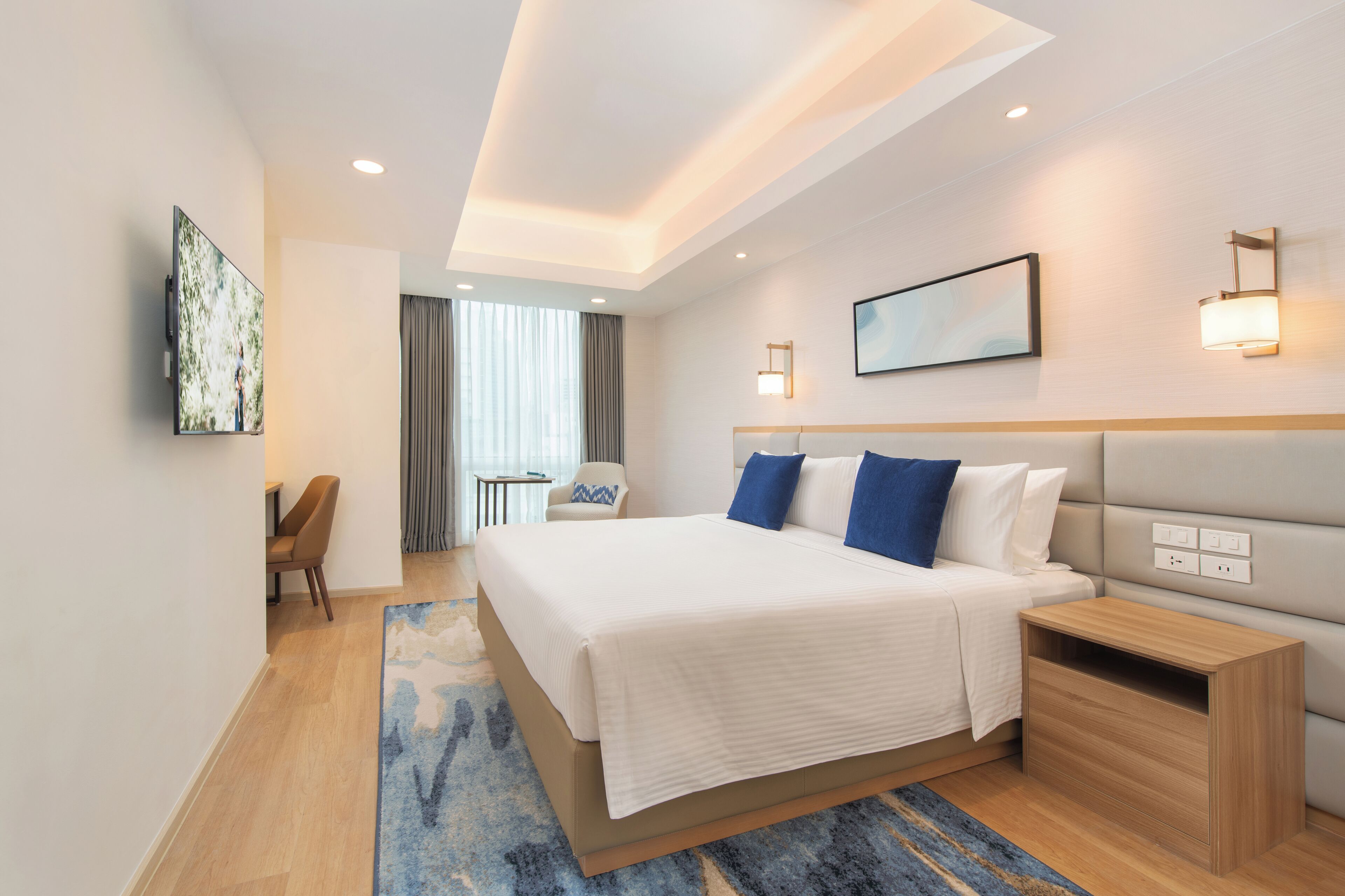 A modern hotel room with a large bed, bedside tables, a desk, and a view of the city.