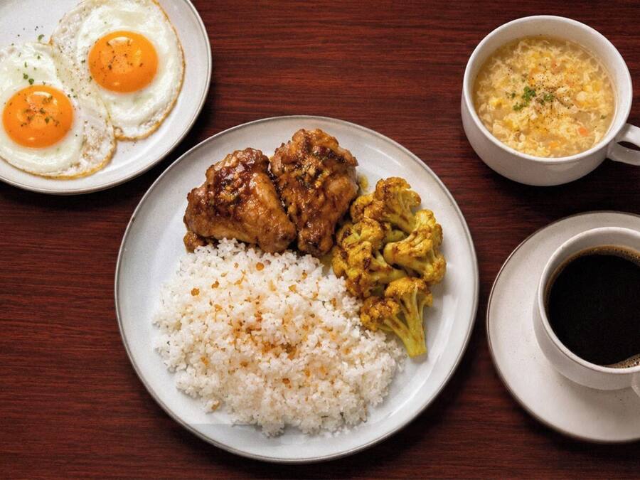 A plate of food with rice, chicken, and vegetables, a cup of coffee, and a bowl of soup.