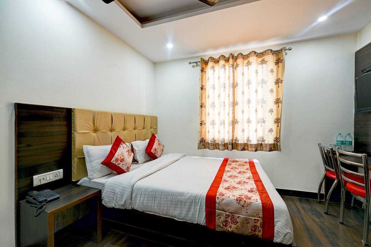 Een hotelkamer met een bed, een nachtkastje met een telefoon, een raam met gordijnen en een bureau met stoelen.