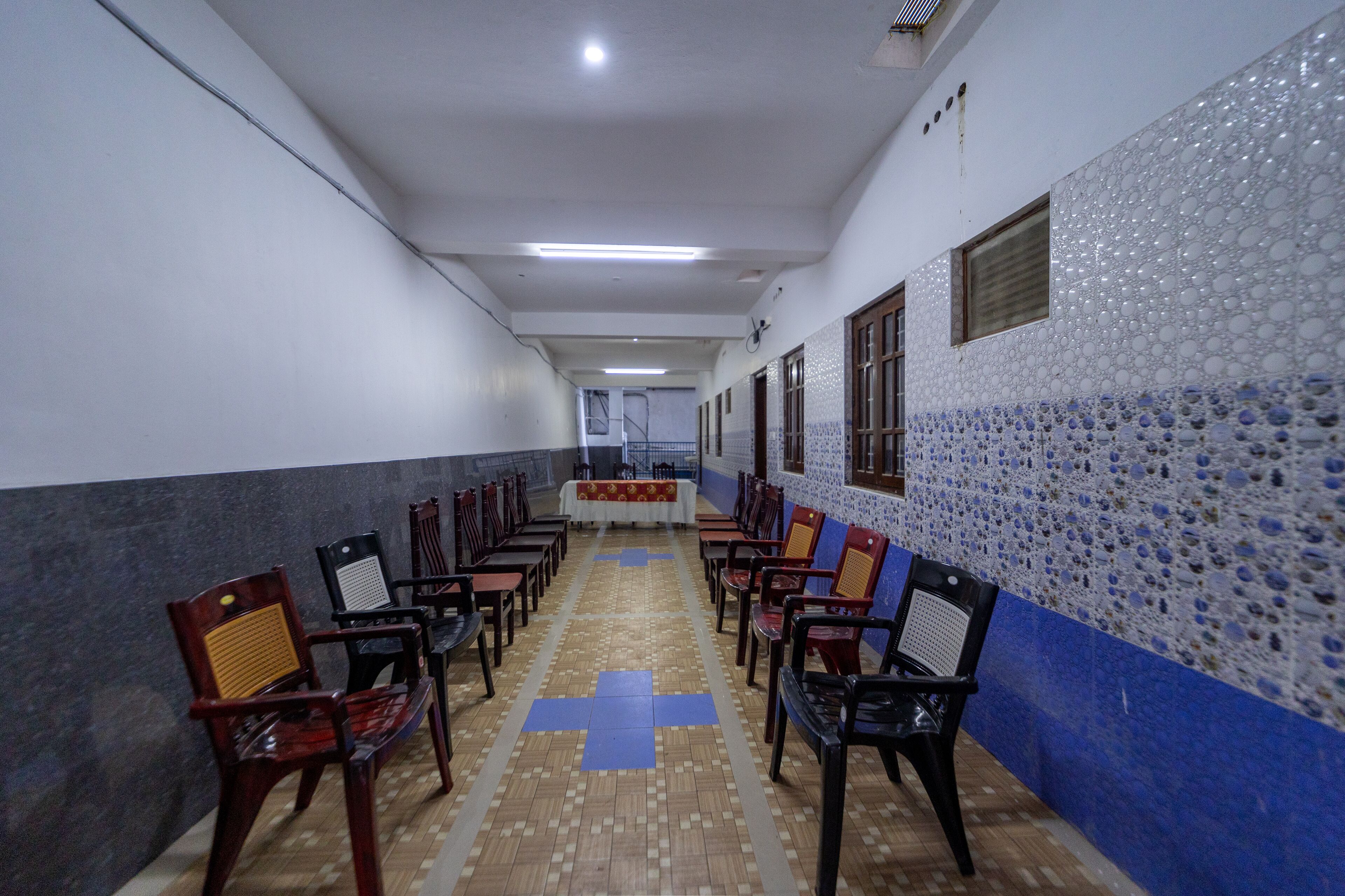 Un pasillo flanqueado por filas de sillas de madera, que conduce a un área central con una mesa y sillas.