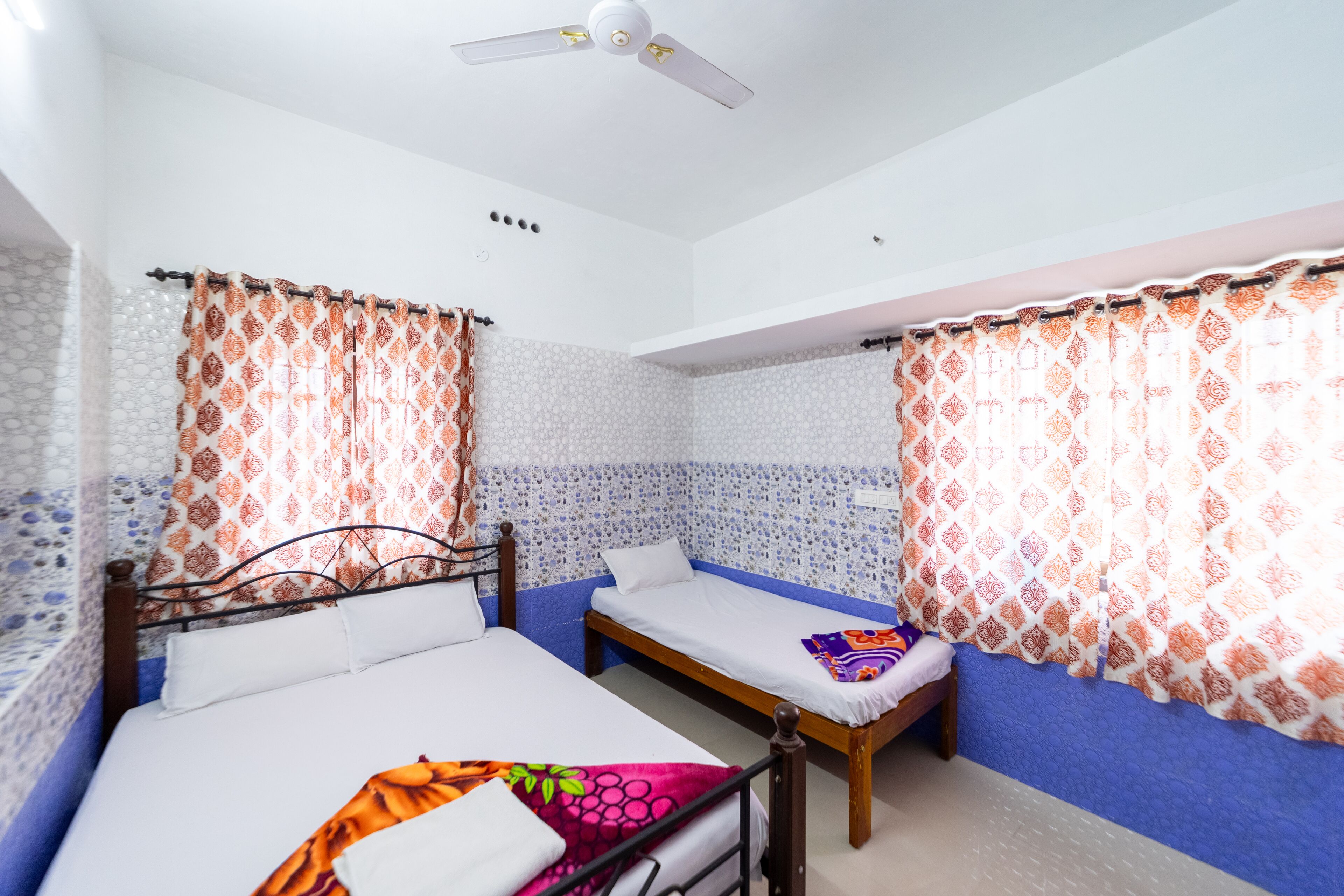 A room with two beds, a ceiling fan, and patterned curtains.