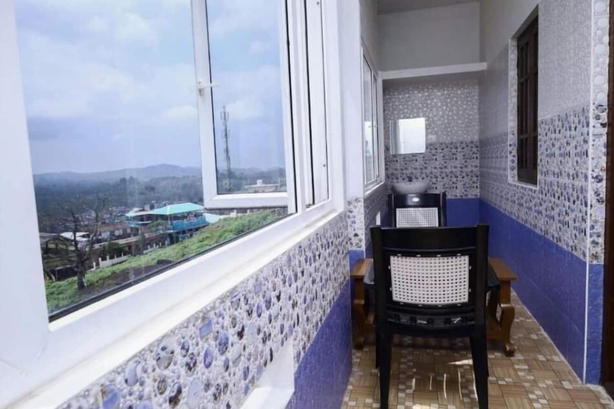 A balcony with a view of a distant town, a tiled wall, and a chair.