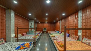 Habitación de hotel con un largo pasillo, techo de madera y varias camas con ropa de cama colorida.