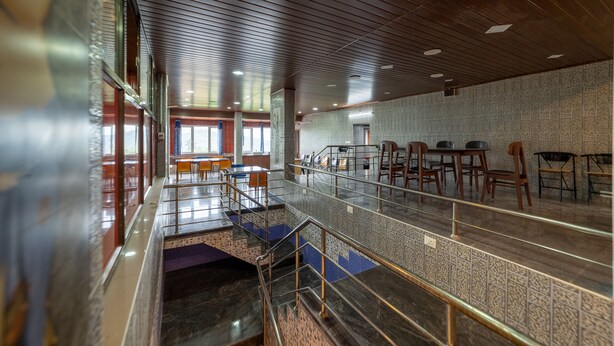 Un espacioso vestíbulo de hotel con techo alto, una escalera central y una zona de estar con mesas y sillas.