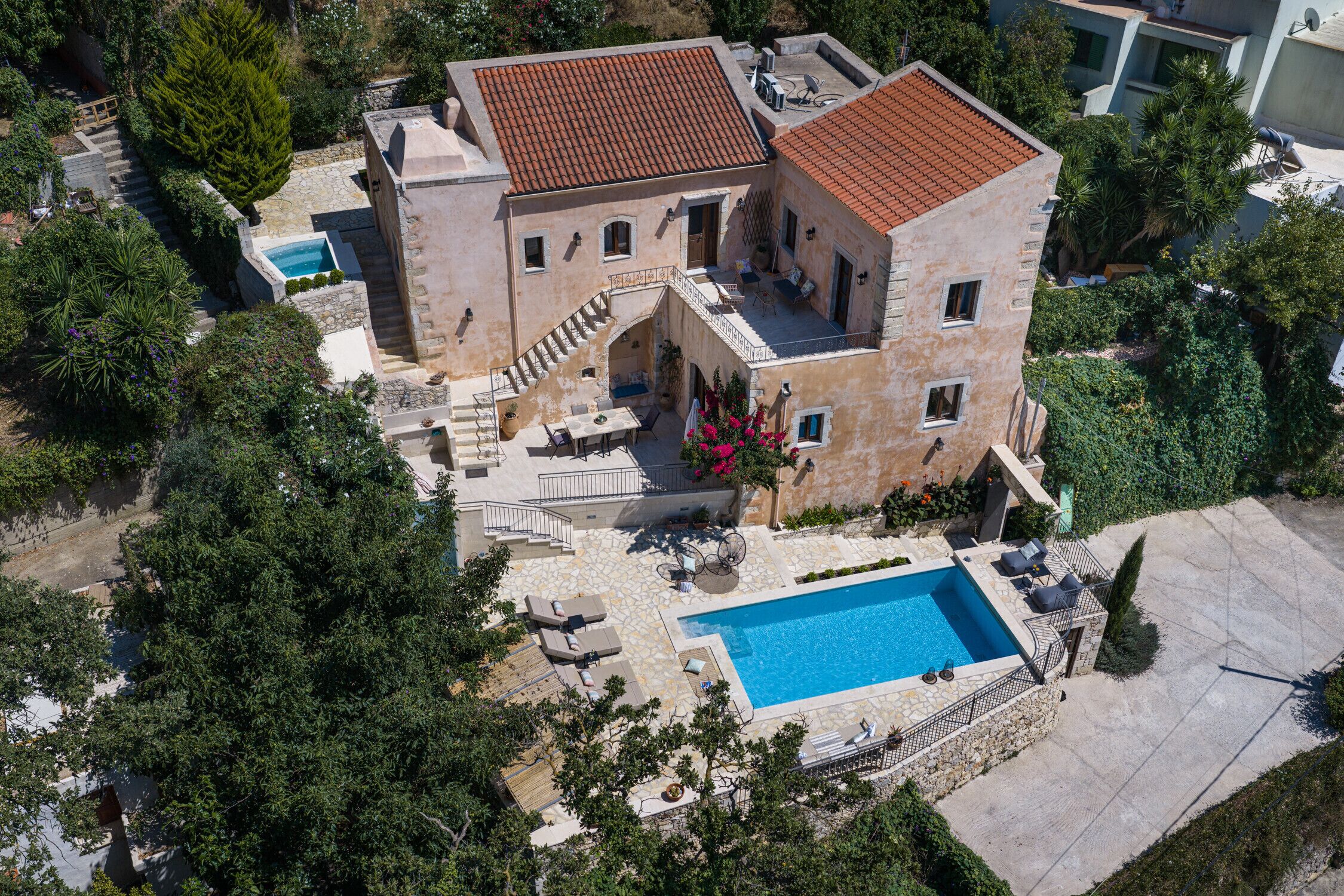A two-story building with a swimming pool, outdoor seating, and a staircase leading to a terrace.