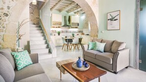 A living room with a stone archway, a sofa, a coffee table, and a kitchen in the background. - Butterfly, a historical, fairytale-style, villa with pool & hot tub! (Armeni)