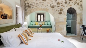 A cozy bedroom with a stone wall, a green sofa, a bed with striped pillows, and a small table with a vase. - Butterfly, a historical, fairytale-style, villa with pool & hot tub! (Armeni)