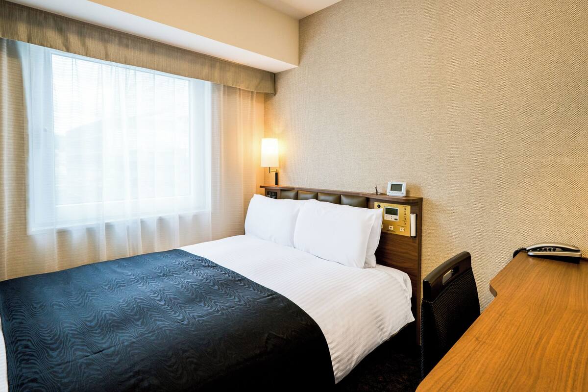 A hotel room with a large bed, a bedside table with a phone, and a window with curtains.