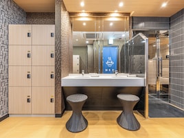 Un baño moderno con un espejo grande, dos taburetes y el letrero de baño público.