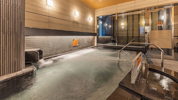 A modern bathroom with a wet floor, tiled walls, and a wooden bench. - APA Hotel Hiroshima Ekimae Shinkansenguchi (Hiroshima)