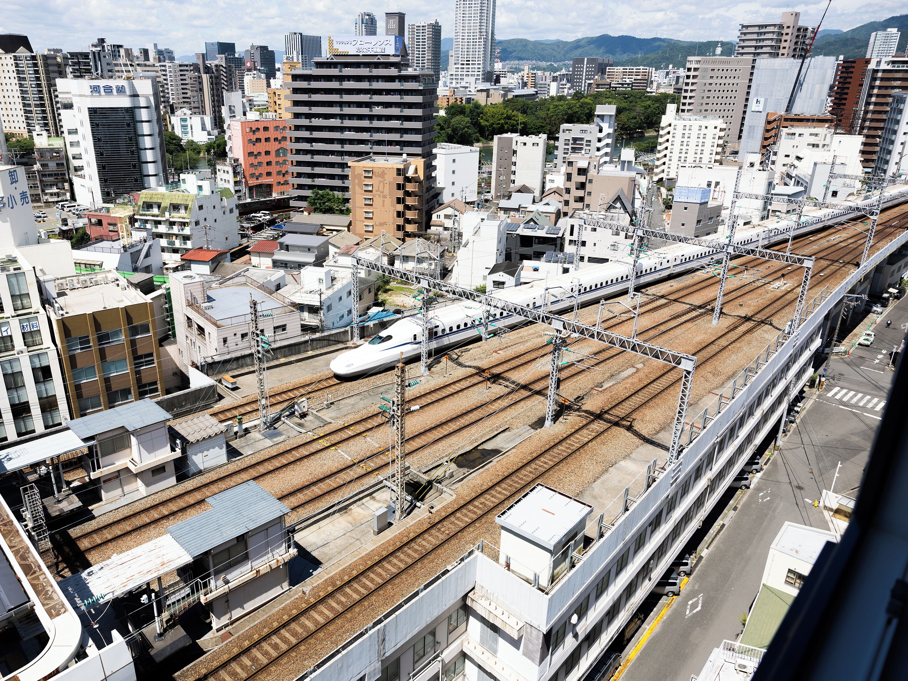 A high-speed train on tracks with multiple levels of infrastructure, surrounded by urban buildings.