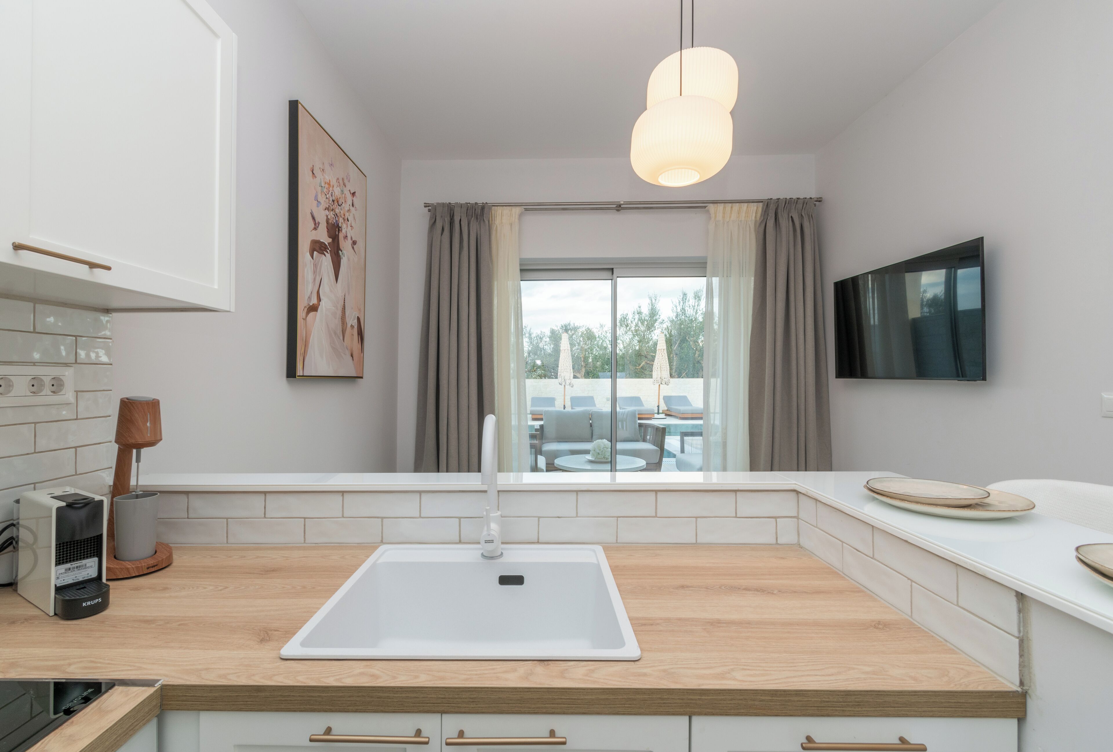Une cuisine moderne avec un plan de travail en bois, des armoires blanches, un évier encastré et un luminaire suspendu.