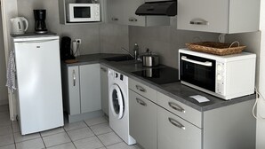 Une cuisine compacte équipée d’un lave-linge, d’un four à micro-ondes et d’une machine à café.