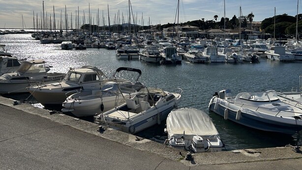 Un port de plaisance où de nombreux bateaux sont amarrés, un ciel dégagé et une surface d’eau calme.