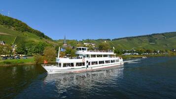 A riverboat with multiple decks, surrounded by lush green hills and a clear blue sky.