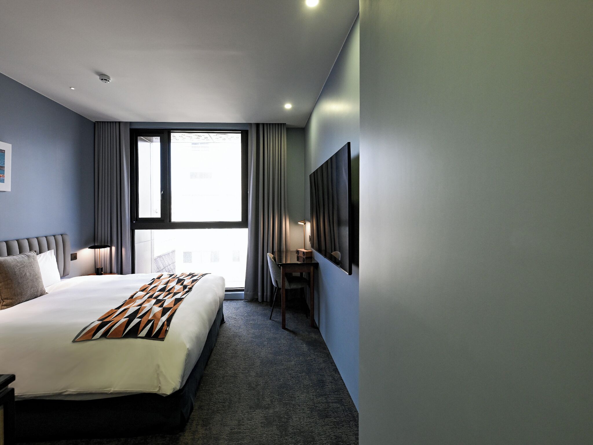 Une chambre d’hôtel avec un grand lit, un bureau, une chaise et une grande fenêtre.