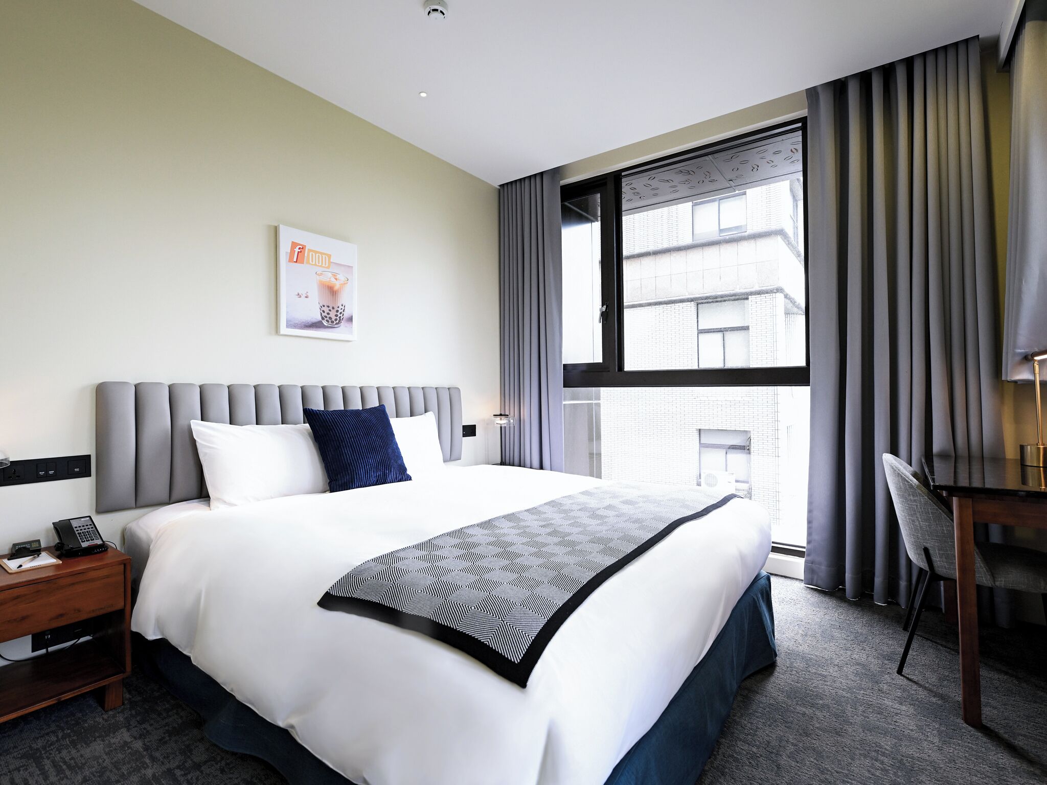 A hotel room with a large bed, a desk, and a window with curtains.
