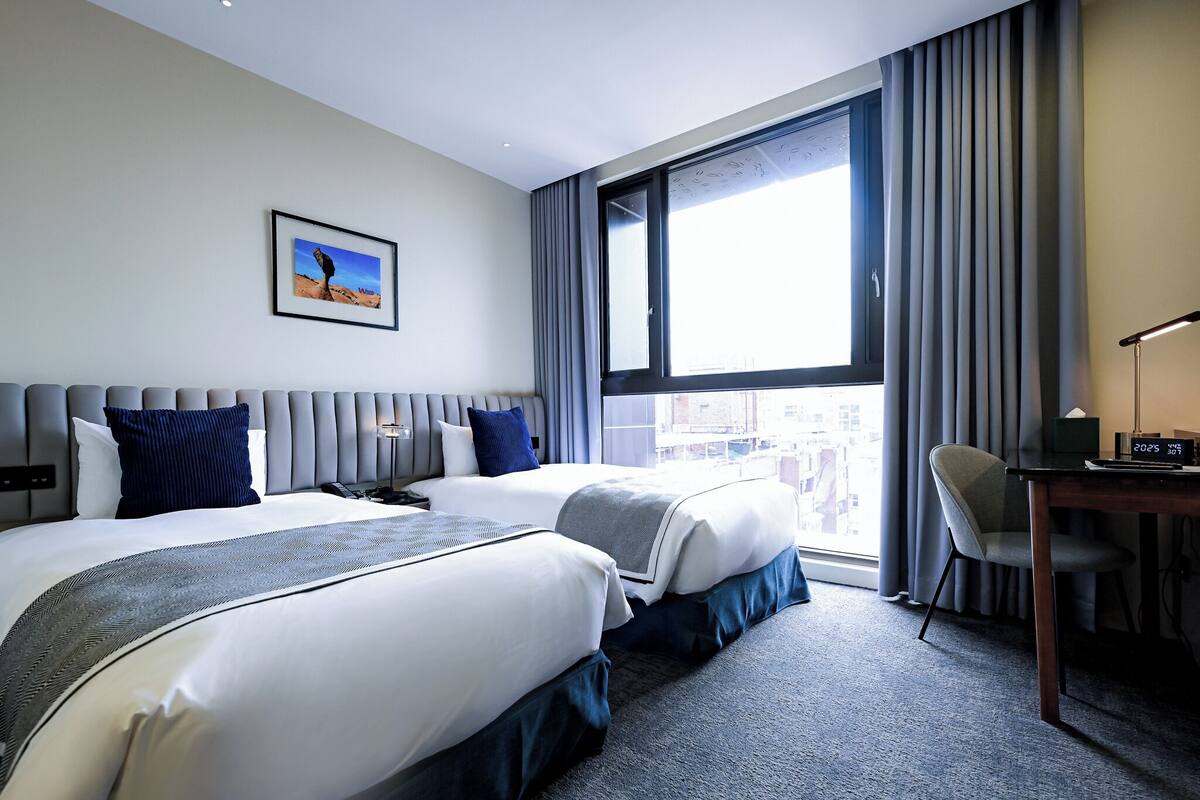 A hotel room with two beds, a desk, and a chair.
