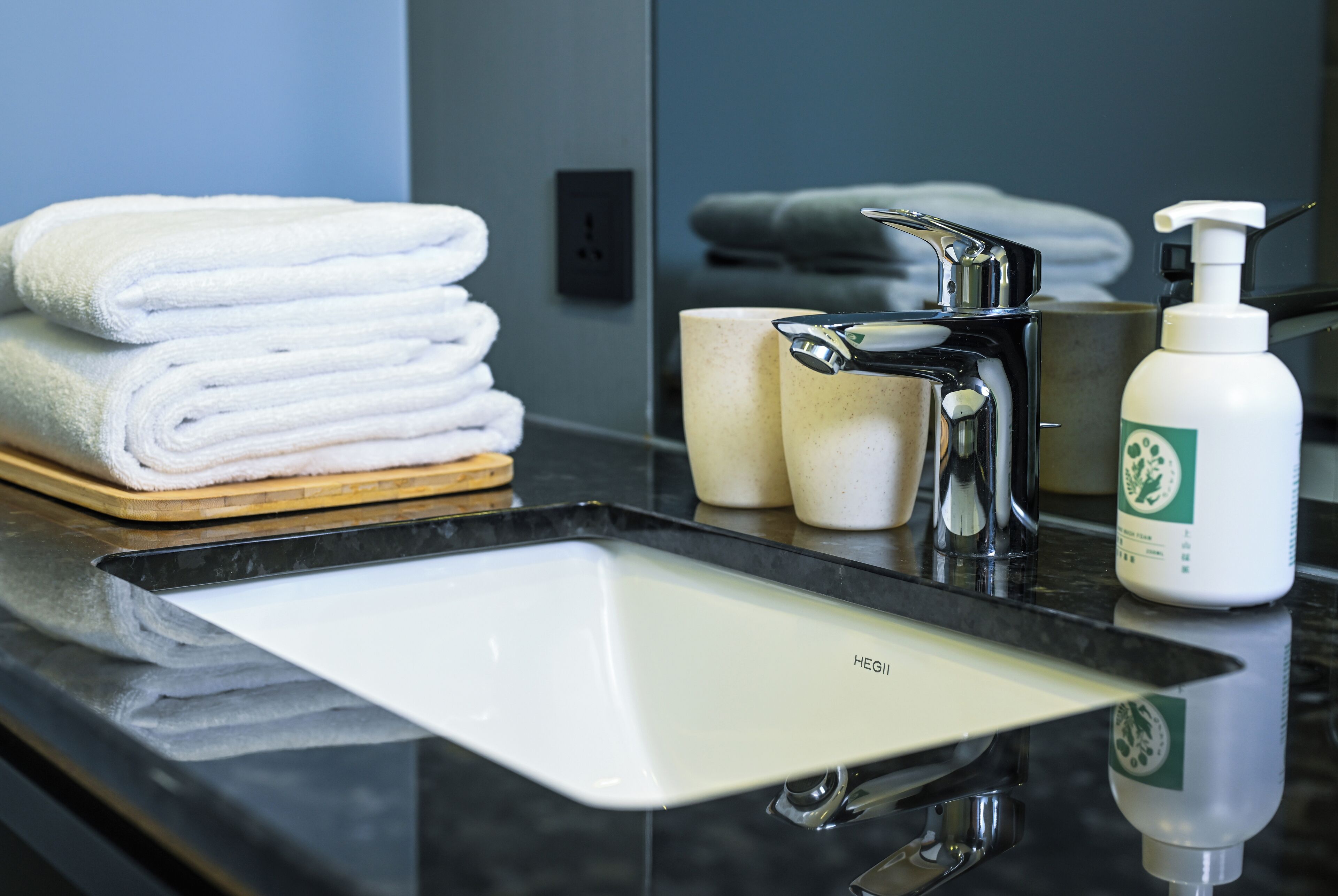 A bathroom with a black countertop, a white sink, a stack of white towels, a soap dispenser, and a mirror.