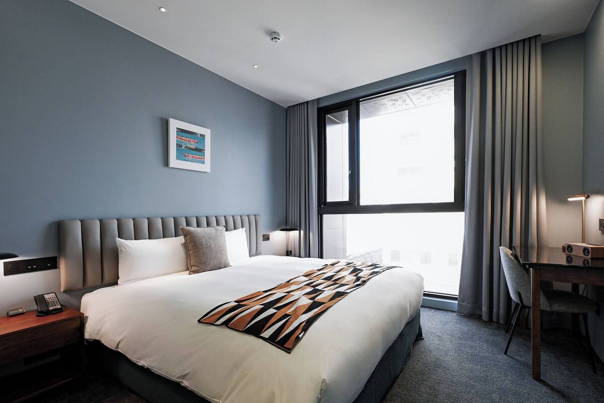 A modern hotel room with a large bed, a desk, and a window with curtains.