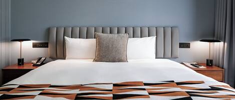 A neatly made bed with a patterned blanket, a grey upholstered headboard, bedside lamps, and a framed picture above the bed.